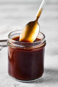 A glass jar filled with stirfry sauce. There is a spoon in the top of the jar with just the tip of of the spoon submerged in the sauce.