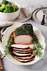 A white plate with a whole pork loin roast on it. There are six slices of pork loin on top of one another on the plate.