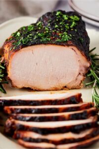 A pork loin on a white plate with slices of it on top of one another on the plate.