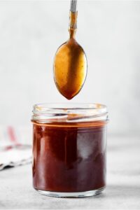 A spoon hovering over a glass jar filled with stirfry sauce,