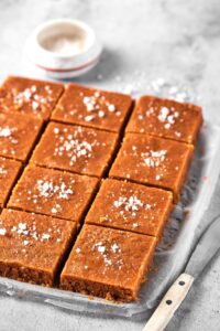 Two rows of four squares of peanut butter fudge on a piece of parchment paper on a gray counter.