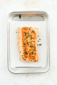 Cooked salmon set on a white sheet of parchment paper in a tin tray.