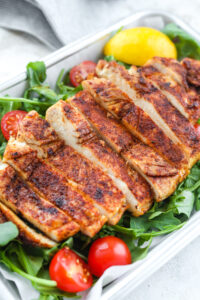 A cooked chicken breast set on top of arugula.