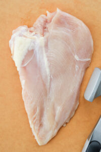 An uncooked chicken breast on a cutting board.