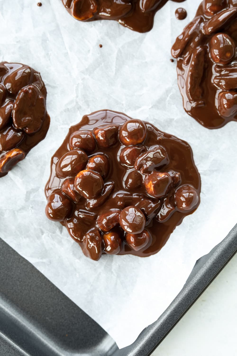 Melted chocolate and nuts spooned onto a baking sheet lined with parchment paper.