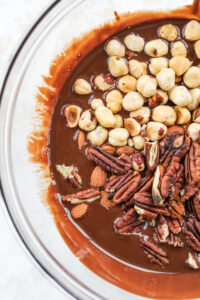 A clear glass bowl filled with melted chocolate and mixed nuts.