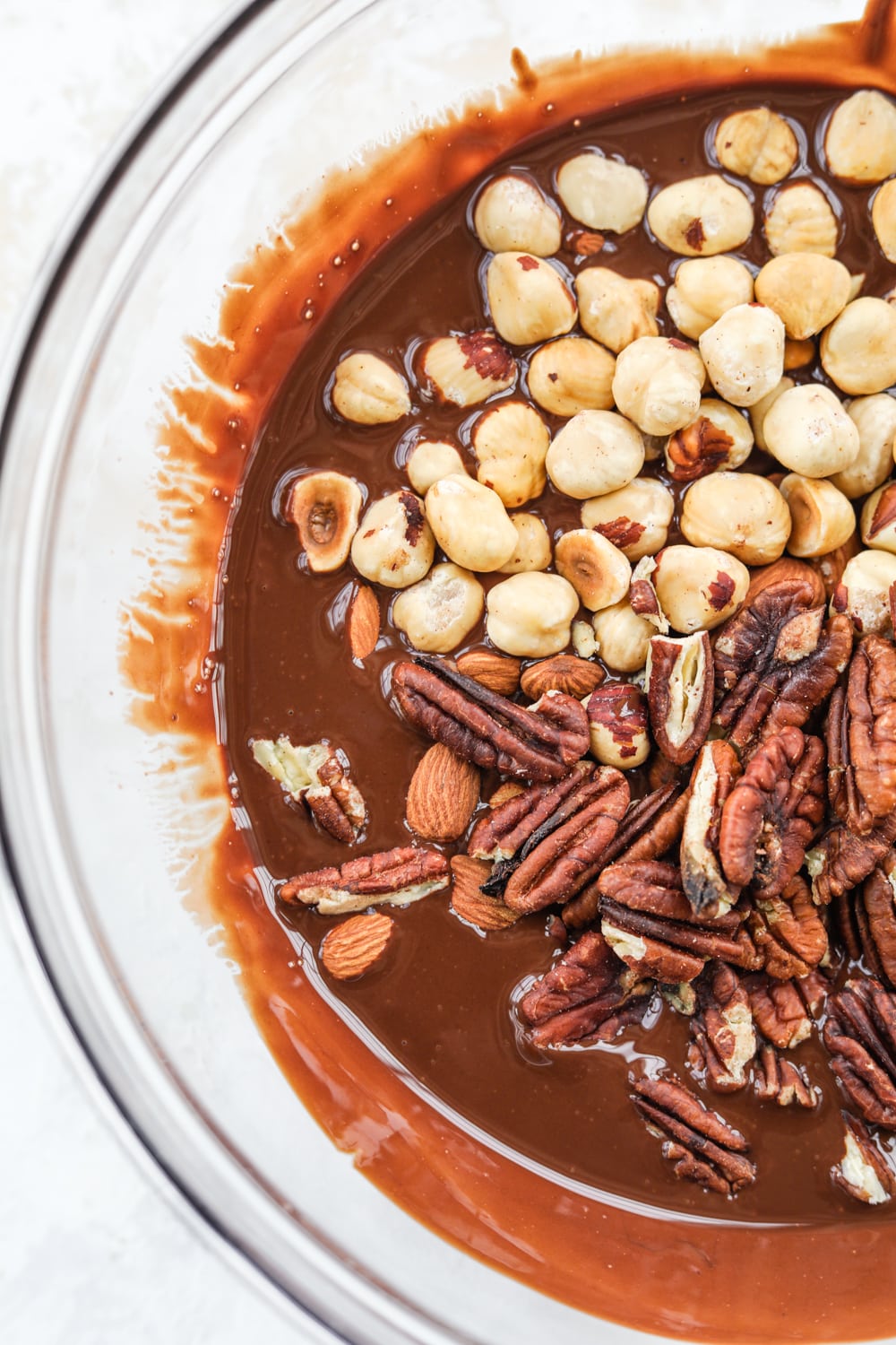 A clear glass bowl filled with melted chocolate and mixed nuts.