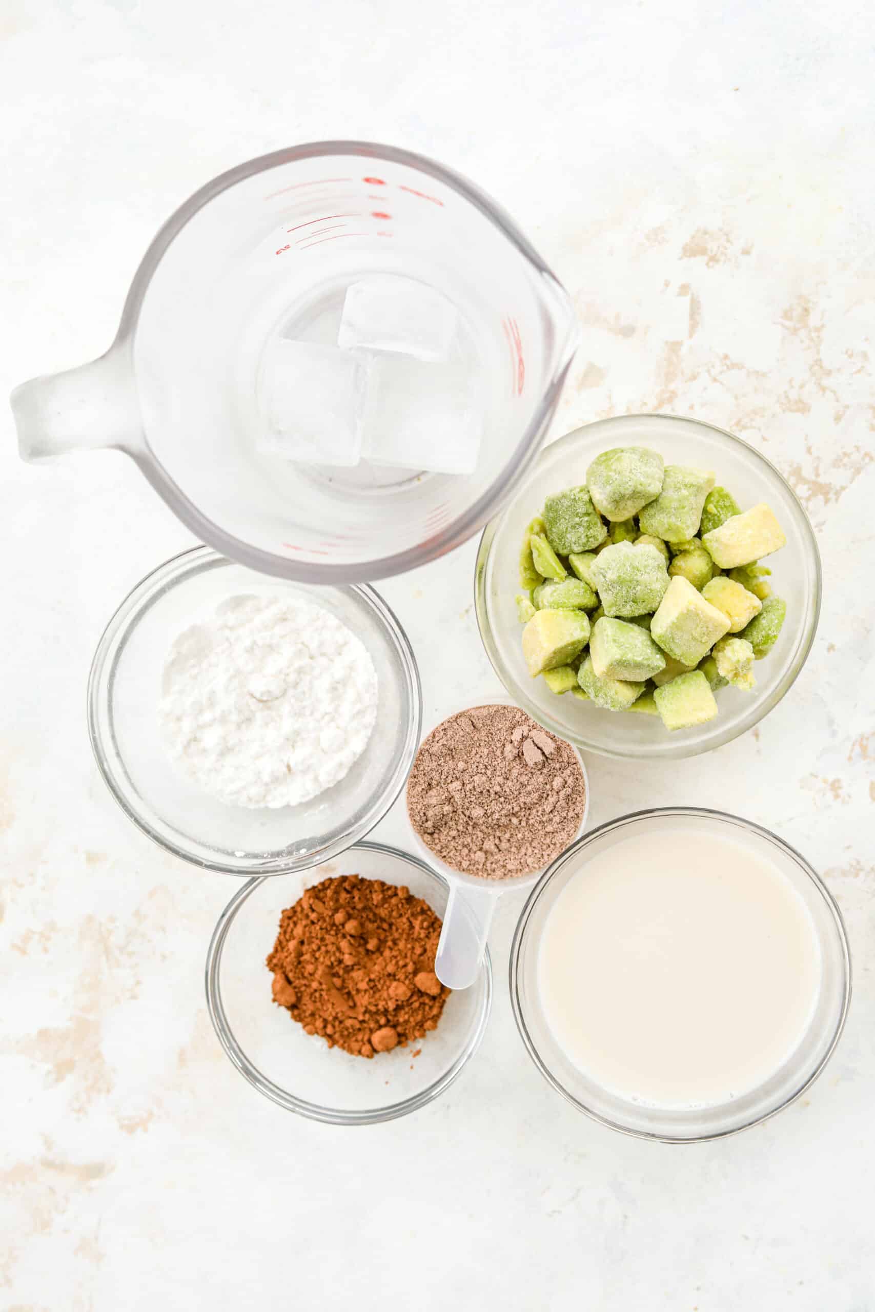 Clear ramekins with a variety of ingredients inside of them set on a white table.