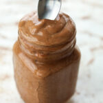 A spoon being dipped inside of a glass jar that's full of a chocolate frosty.