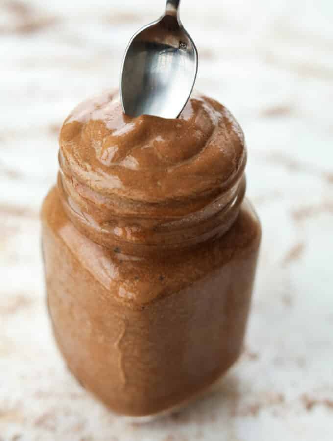 A spoon being dipped inside of a glass jar that's full of a chocolate frosty.