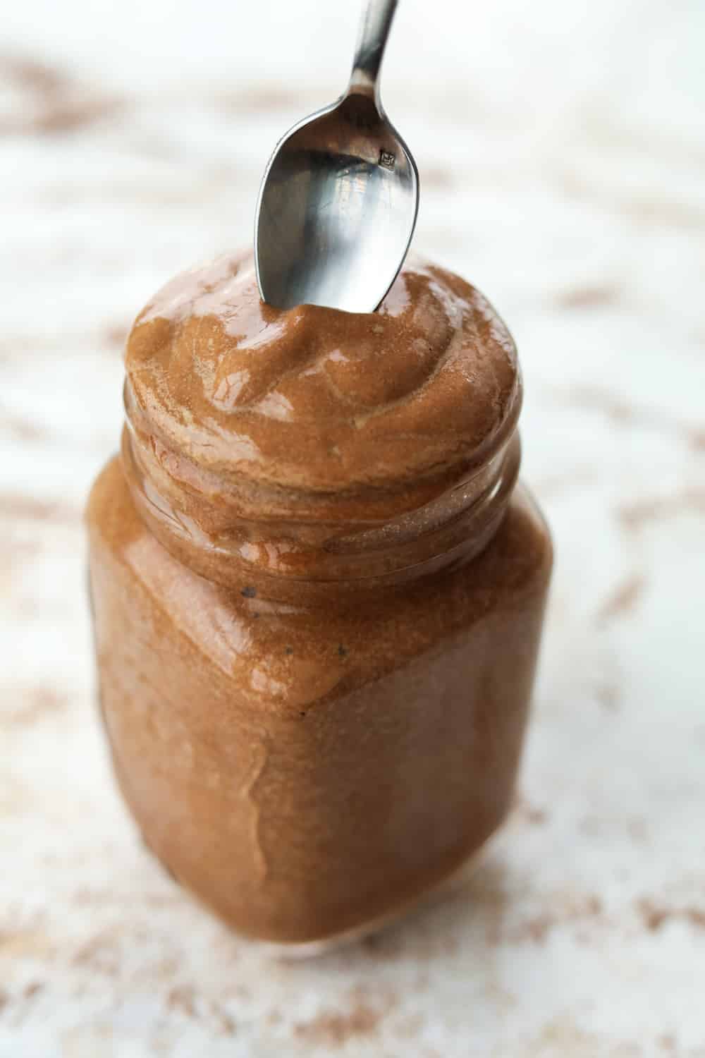 A spoon being dipped inside of a glass jar that's full of a chocolate frosty.