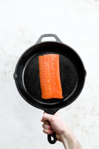 A raw filet of salmon in a cast iron pan.