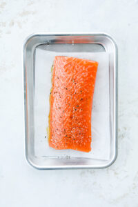 Raw salmon coated in olive oil salt and pepper. The salmon is placed in a tray lined with parchment paper.