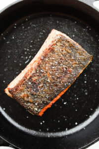 A black cast iron pan with a cooked salmon filet set inside of it.