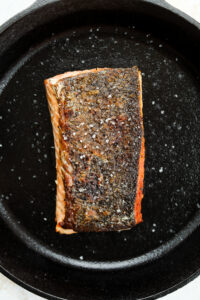 A cooked salmon filet with the skin side facing upwards in a black cast iron pan.