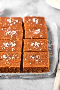 Two rows of four squares of peanut butter fudge on a piece of parchment paper on a baking sheet on a gray counter.