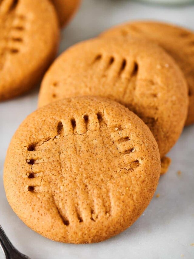 Three peanut butter cookies overlapping one another and a white counter.