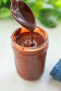 A spoon dripping homemade nutella into a glass jar.