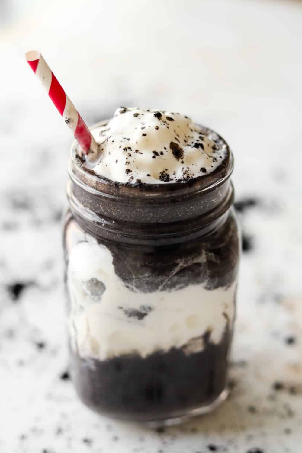 An Oreo flavored protein shake in a glass mug. There's a red and white straw in the mug.