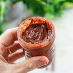 A hand holding a glass jar full of healthy Nutella.