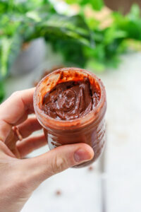 A hand holding a glass jar full of healthy Nutella.