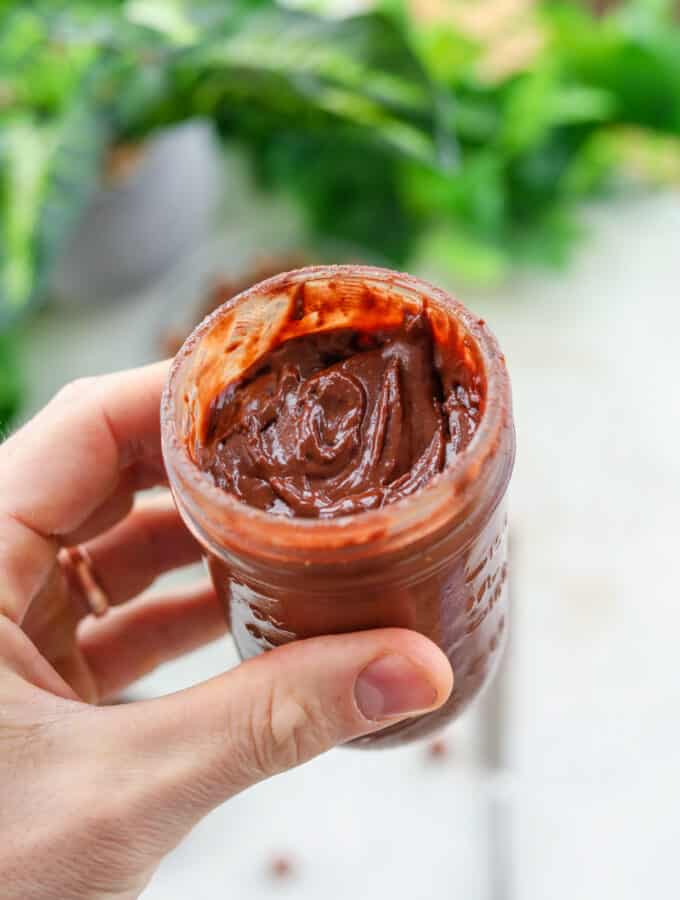A hand holding a glass jar full of healthy Nutella.