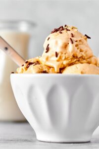 Part of a white bowl with two scoops of almond milk ice cream with another scoop on top.
