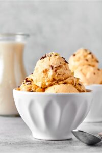 White bowl with a couple scoops of almond milk ice cream in it. Behind it is part of another ball scoops of ice cream and part of a glass jar with almond milk.