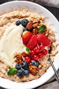 Blueberries, strawberries, red currants, pecans, and cream cheese on top of oatmeal in a white bowl.