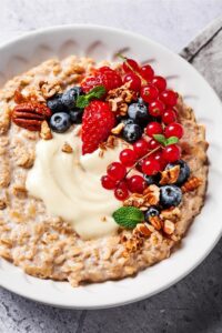 Oatmeal in a white bowl with cream cheese, blueberries, strawberries, red currants, and pecans on top of it.