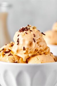 Scoop of almond milk ice cream on top of a few more scoops in part of a white bowl.