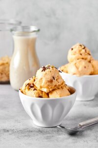 A white bowl with a couple scoops of almond milk ice cream in it. Behind it is another bowl with scoops of ice cream next to that is a glass jar filled with milk.