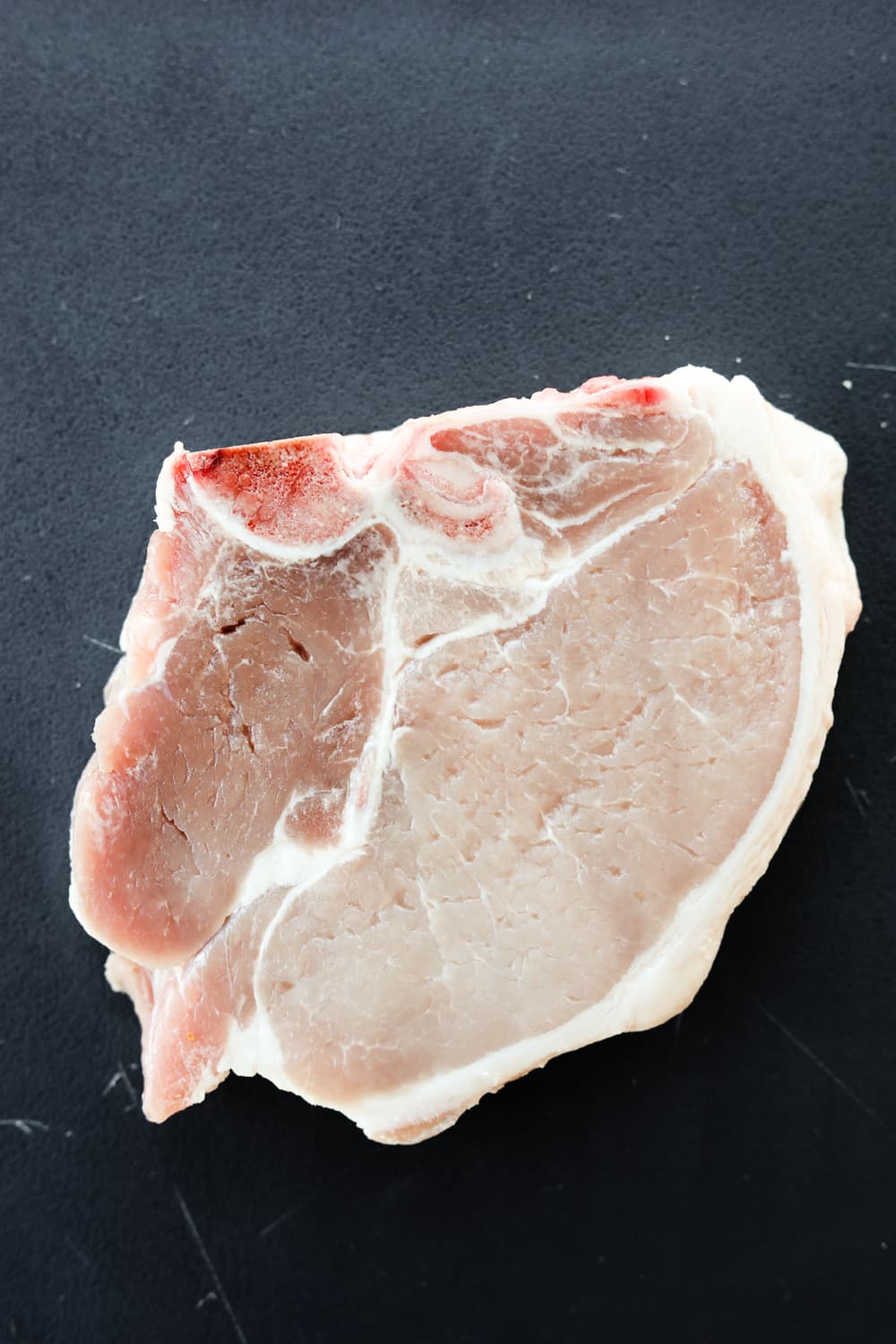 An uncooked pork chop on a black cutting board.