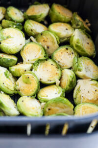 Seasoned halved brussels sprouts in a black air fryer basket.