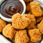 Keto chicken nuggets on a tin serving tray next to a white cup of barbecue sauce.