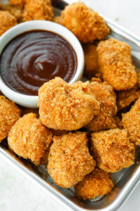 Keto chicken nuggets on a tin serving tray next to a white cup of barbecue sauce.