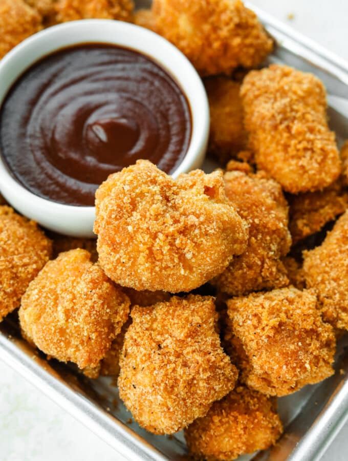 Keto chicken nuggets on a tin serving tray next to a white cup of barbecue sauce.