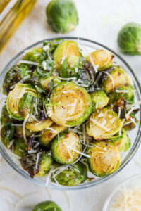 A bowl of roasted brussels sprouts topped with Parmesan cheese and flaky salt.