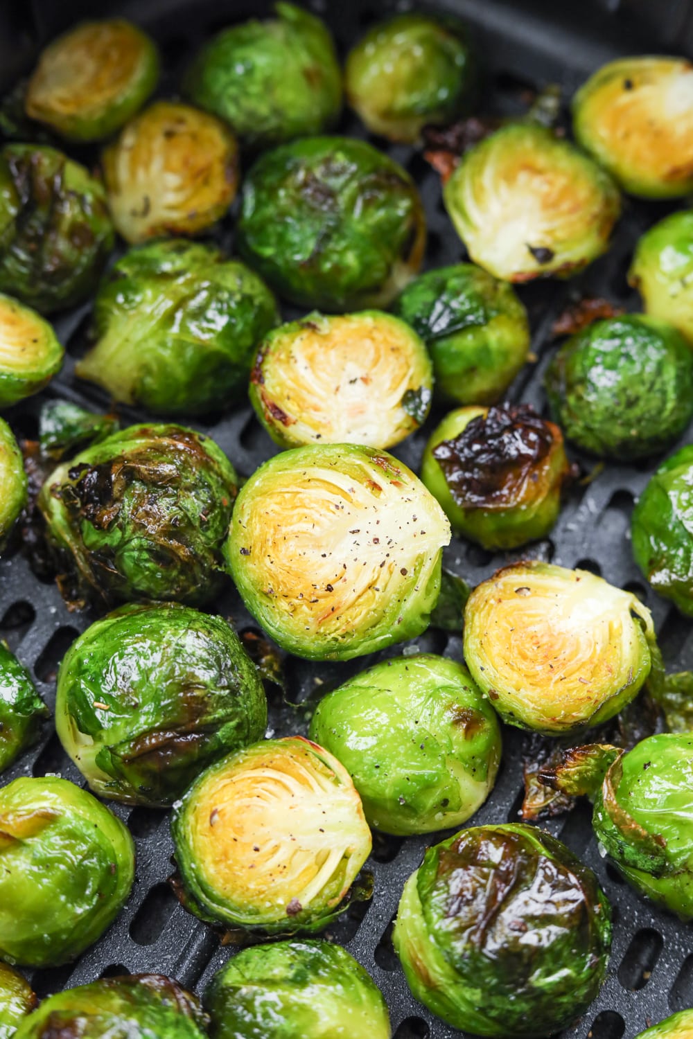Roasted brussels sprouts in a black air fryer basket.