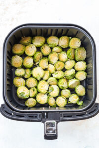 An air fryer basket full of uncooked halved brussels sprouts.