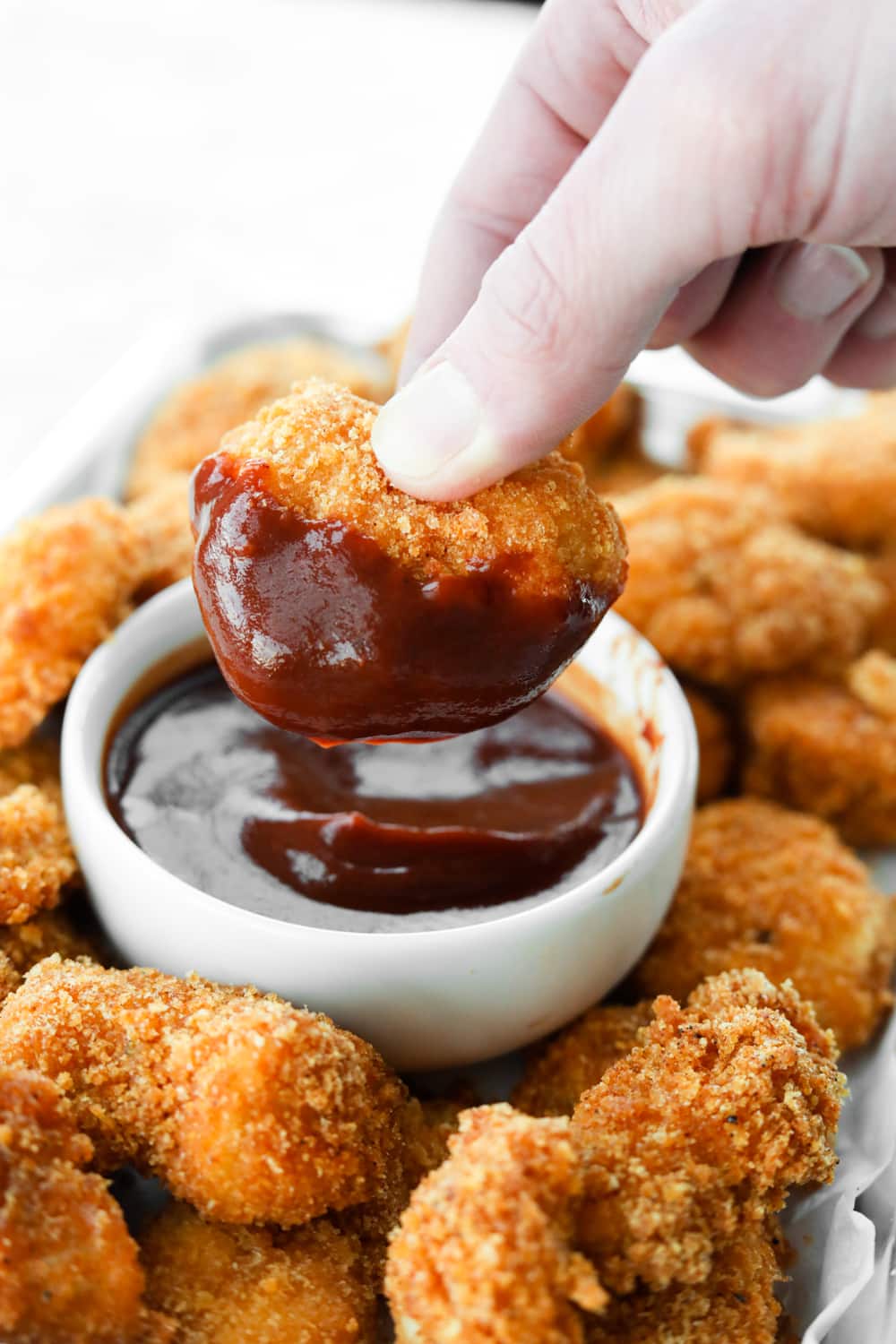 A hand holding a chicken nugget that's been dipped in barbecue sauce.
