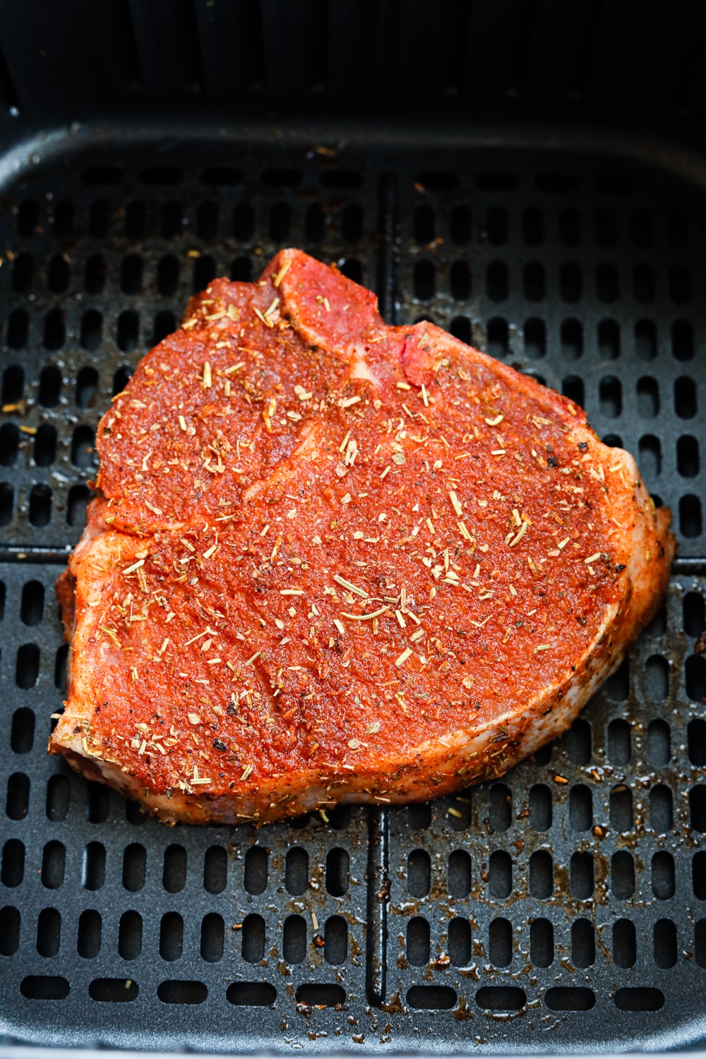 An uncooked pork chop covered in dry rub set an air fryer basket.