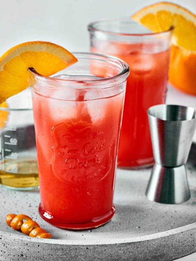 And two glasses of sex on the beach with an orange slice on the rim, a alcohol measure, and a glass of liquor all on a silver circular serving dish.