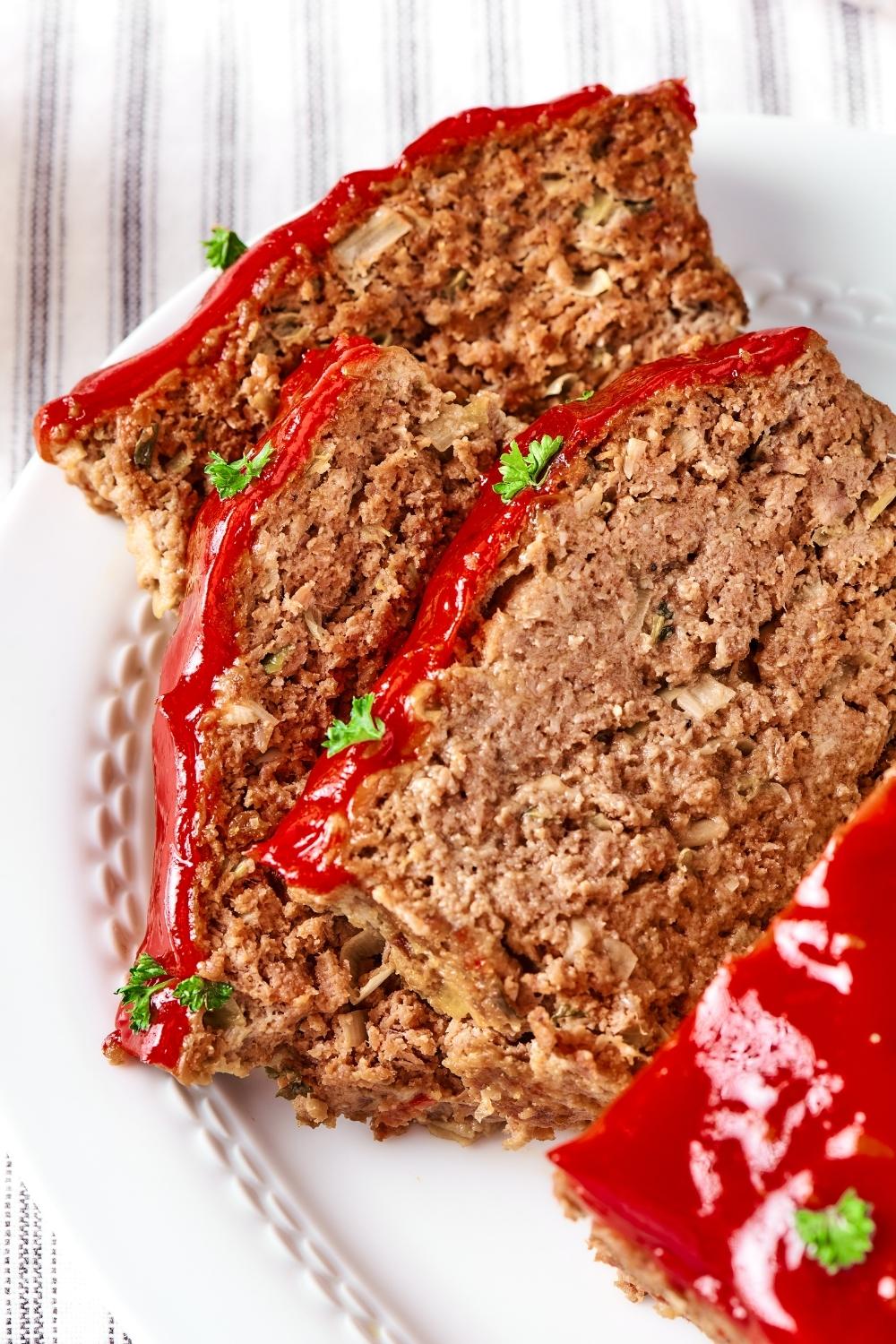 Three slices of meatloaf overlapping one another on a white plate.