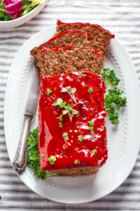 Meatloaf on a white plate with three slices cut out from the front of it that are lying on top of one another on the plate.