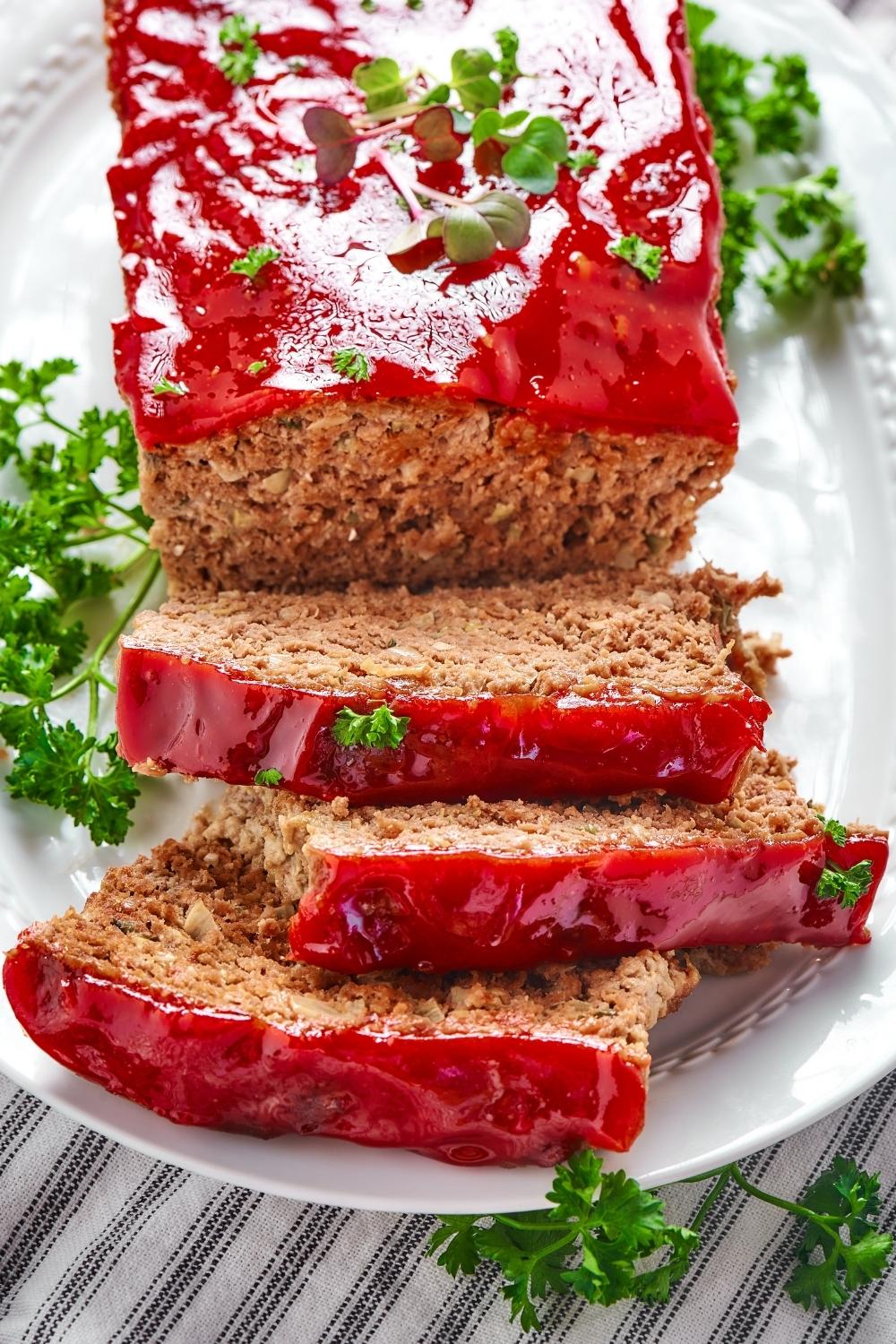 Three slices of meatloaf on top of one another on a white plate. The slices are touching part of the whole meatloaf.