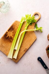 Three stalks of celery on a wooden cutting board on the way counter.