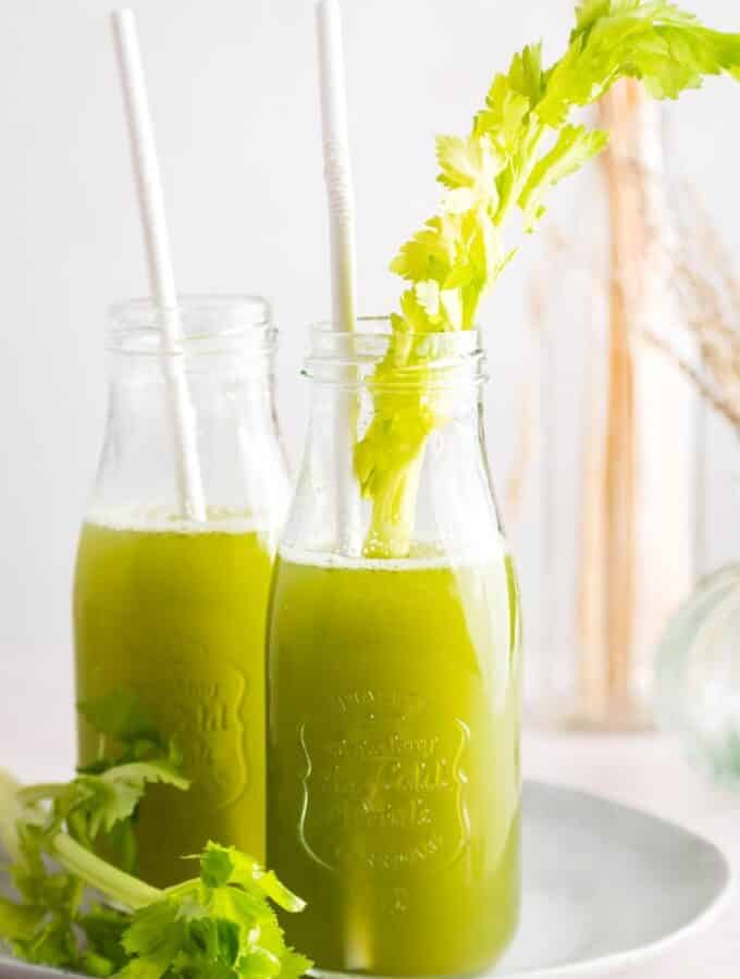 To Glasses filled with celery juice with straws in them. The glasses are on a white plate on a white.