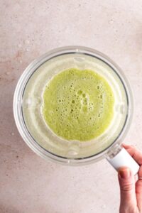 Hand holding a blender that is filled with celery juice.