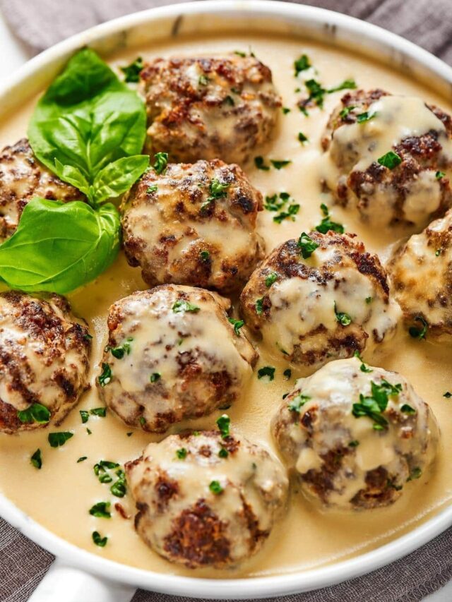 A bunch of gluten-free meatballs covered and gravy on a plate that has a white gravy on it.